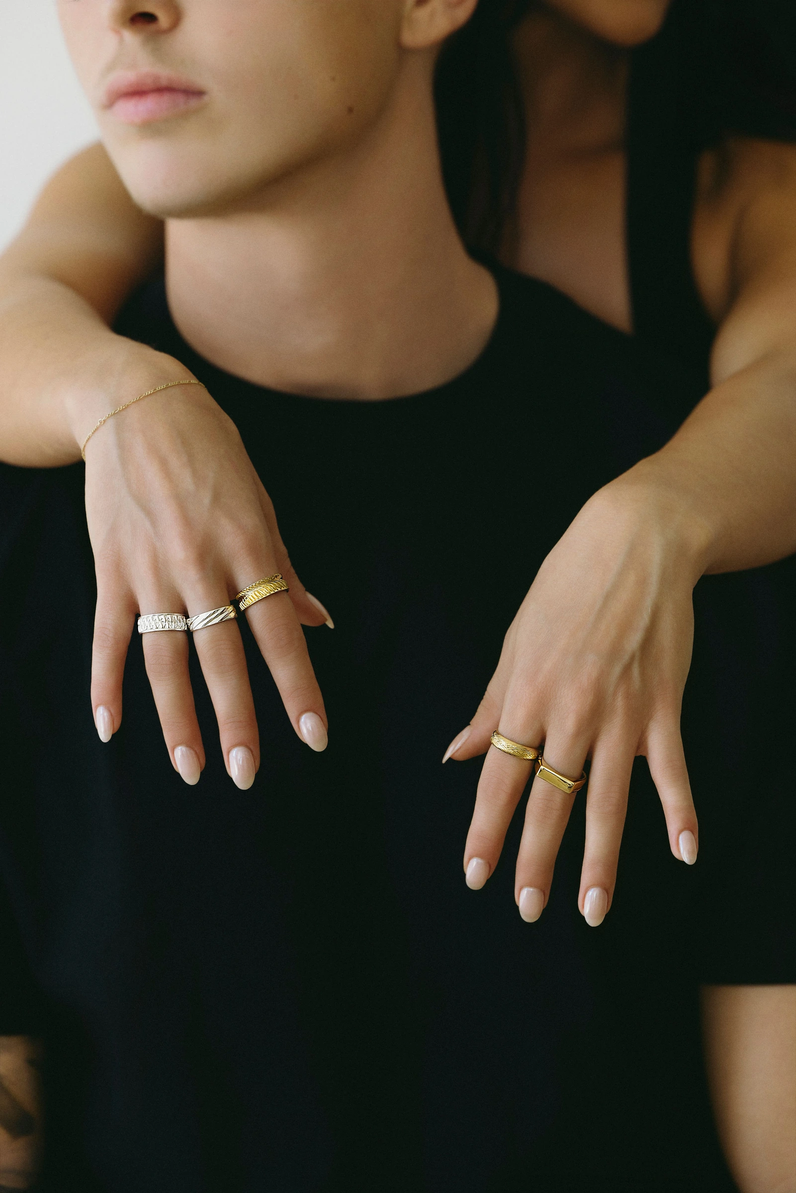 Two models wearing rings, hands resting over a black shirt