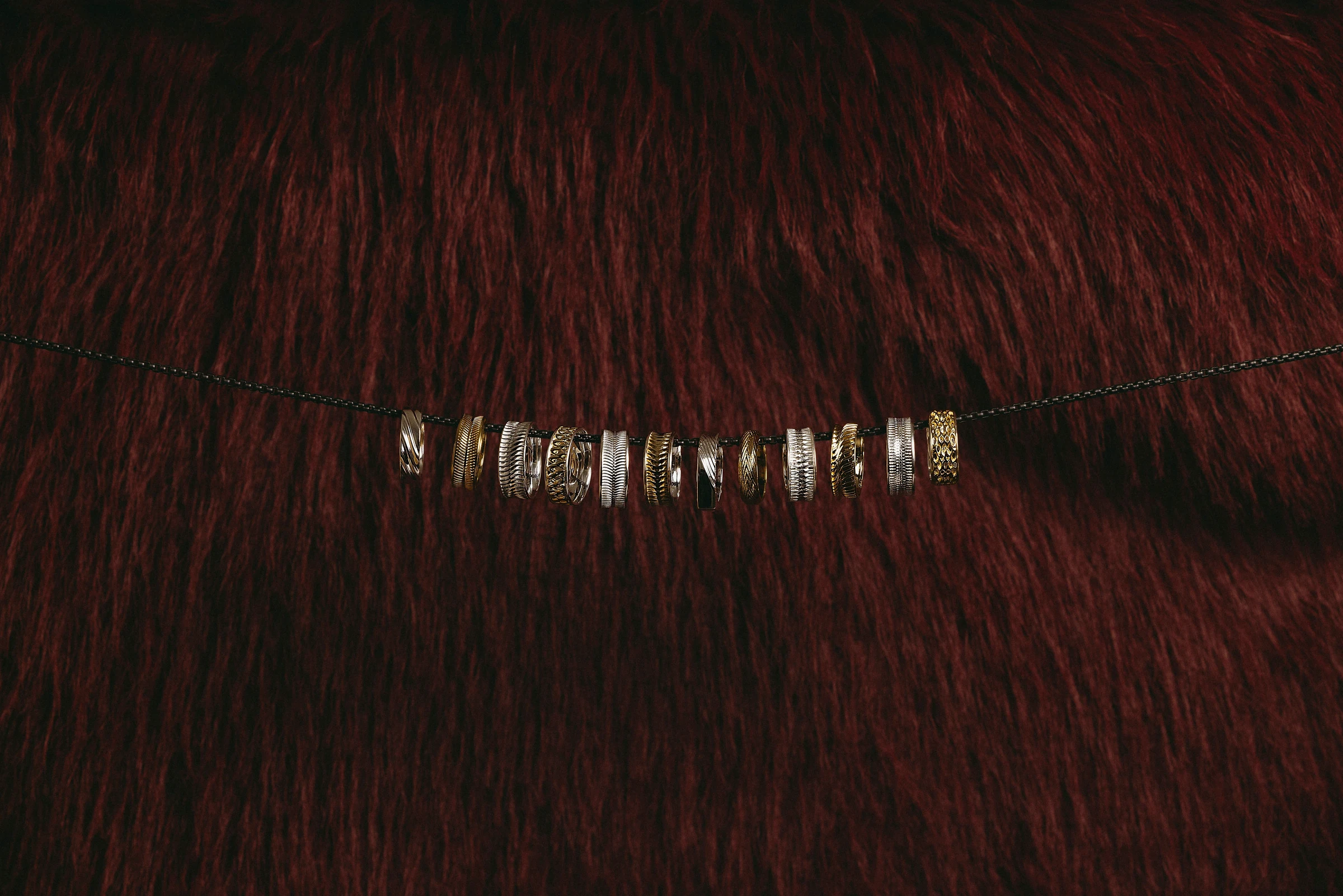 The launch collection rings strung on a fine cord across burgundy fur, wide view